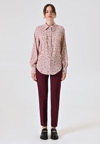 Camicia a maniche lunghe, con bottoni, di colore rosa chiaro con motivo floreale; abbinata a pantaloni borgogna aderenti e scarpe nere con dettaglio in catena.