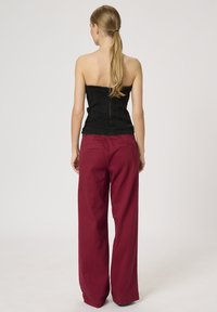 Must musta korsett, mis on varreta ja seljaosal tõmbetõmbe lukuga, koos vabalt istuvate burgundy värvi pükstega. Sile tekstuur, struktureeritud disain ja minimalistlik stiil.