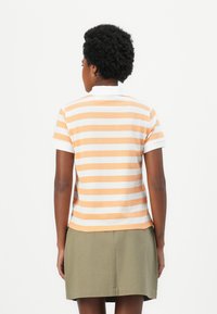 Korte mouwen polo-shirt in oranje en witte strepen, gemaakt van katoen, met een witte kraag en een rechte zoom. Draagt bij een khaki rok.