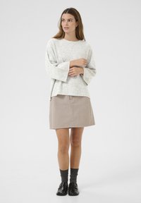 Lichtgrijze, gestructureerde trui met brede mouwen, gecombineerd met een beige rok met zijknopen. Donkergrijze sokken en zwarte loafers maken de look compleet.