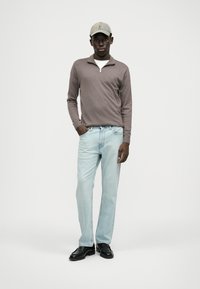 Heledpruun tõmblukuga kootud särk, valge aluspesu, helesinised teksad, mustad jalanõud ja heledat halli värvi pesapalli müts. Mudel seisab valge tausta vastas.