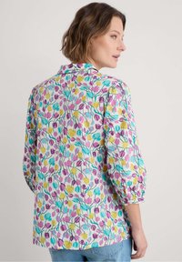 Blusa floral con un fondo azul claro y patrones de tulipanes rosas y amarillos, mangas tres cuartos y un diseño de cuello clásico.