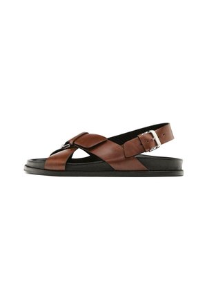 Bruine leren sandalen met kruisbanden, een hielband en een zilveren gesp; platte zwarte zool met een gladde textuur en een minimaal ontwerp.