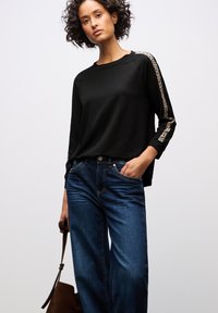 Svart långärmad topp med leopardtryck på ärmarna, kombinerad med blå vida jeans. Outfiten har en avslappnad design och en lös passform.
