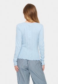 Světle modrý svetr s dlouhým rukávem, s vzorovou strukturou, žebrovanými detaily a přiléhavým střihem. Volánkový lem a rukávy po lokty.