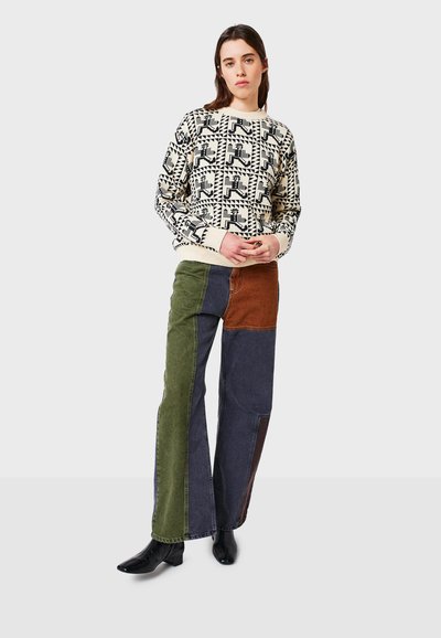 Maglione con motivo geometrico nero e crema, abbinato a pantaloni in denim a patchwork multicolore nei toni del verde, marrone e blu, completato da stivali neri.