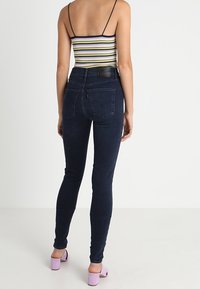 Jeans ajustados azul oscuro con una cintura alta, hechos de denim. La parte trasera presenta costuras de bolsillo y una etiqueta de cuero, combinados con una blusa a rayas.