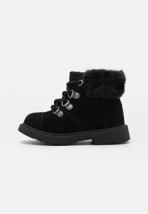 Black ankle boot with suede texture, fur collar, metal eyelets, and thick rubber sole, designed for cold weather.