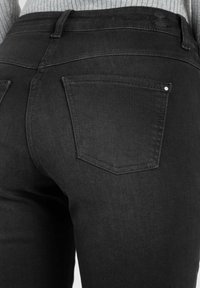 Sorte denimjeans med en tettsittende design, som har to baklommer og subtile sømdetaljer. Materialet ser glatt ut og er litt teksturert.