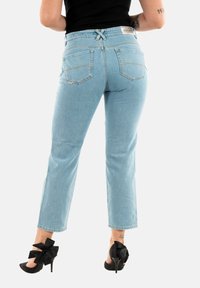 Jeans de tiro alto en azul claro con un corte holgado, que cuentan con dos bolsillos traseros y un detalle decorativo de lazo en la cinturilla.