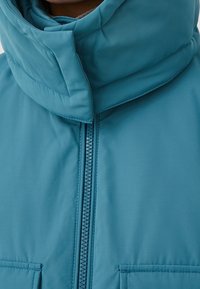 Niebieska kurtka puchowa z wysokim kołnierzem, zamkiem błyskawicznym oraz dwoma przednimi kieszeniami. Tkanina wydaje się gładka i jest widocznie ocieplona.