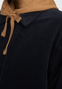 Chaqueta de pana navy con capucha color beige. Presenta un cuello y cierre de traba. La textura es estriada, mostrando finas líneas verticales.