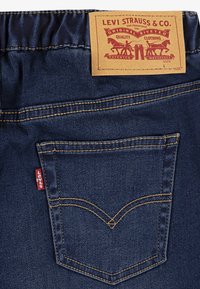 Levi Strauss & Co. denimjeans i blå färg, klassisk design, röd etikett och brun label med en hästlogotyp och varumärkesinformation.