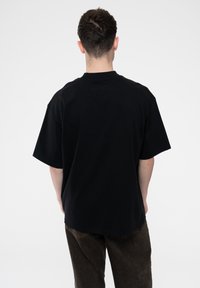 Black cotton t-shirt featuring short sleeves, a crew neck, and a relaxed fit. The back is plain with no visible logos or designs.