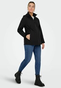 Černá voděodolná bunda se zipem vpředu, kapucí a staženým pasem. V kombinaci s modrými legínami připomínajícími džíny a černými šněrovacími botami.