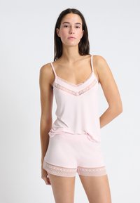 Lichtroze top met kantafwerking, gecombineerd met bijpassende shorts met kantaccenten. Zachte stof, mouwloos ontwerp, relaxte pasvorm.