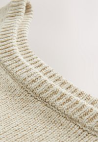 Gros plan sur un tissu en maille côtelée couleur crème avec des motifs de points verticaux texturés.