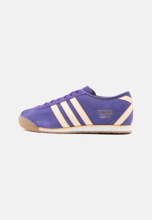 Purple suede athletic shoe with cream-colored stripes, gum rubber sole, and embossed branding on the side. Low-profile design and rounded toe.