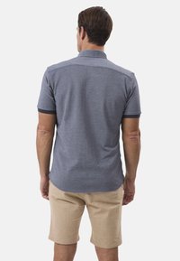 Kortærmet skjorte i heather blå stof med krave, med marineblå accenter på ærmerne, parret med beige shorts.