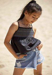 Melnas kokvilnas blūzes ar dekoratīvu šūšanu, saskaņotas ar nolietotām zilo džinsu šortiem, ar plūstošu apakšu un gaišu tonējumu.