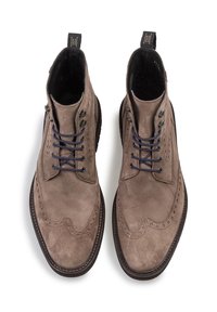 Bottines en suede marron avec un design brogue, bout rond, lacets bleu marine et une languette avec un logo en relief sur le talon.