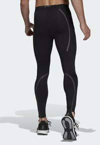 Leggings sportivi neri realizzati in materiale elastico, dotati di linee grigie riflettenti e design aderente, con una fascia in vita ampia e un aspetto elegante.
