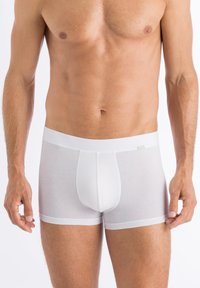 Vita bomullsboxer med en åtsittande design, med en mjuk midjeband och en framficka för stöd, jämn textur genomgående.