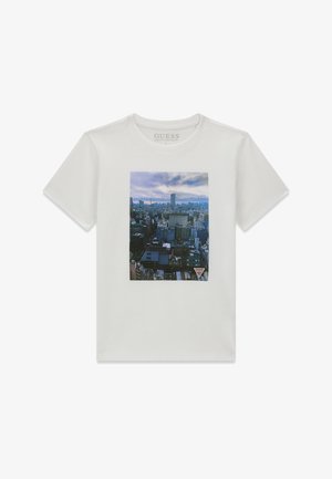T-shirt blanc à manches courtes avec un imprimé photo d'une silhouette de ville sur le devant et un petit logo triangulaire en bas à droite de l'impression.