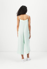 Licht mintgroene, mouwloze jumpsuit met een losse pasvorm, twee voorzakken en verstelbare bandjes. Gemaakt van een gestructureerde, zachte stof.