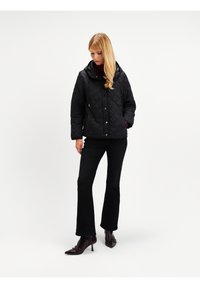 Czarna pikowana kurtka z kapturem, z zapięciem na guziki i bocznymi kieszeniami, połączona z czarnymi spodniami i ciemnobrązowymi szpilkami z ostro zakończonym noskiem.