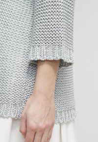 Maglione grigio chiaro a maglia con un motivo testurizzato e un orlo a ondina, dotato di maniche a tre quarti e una vestibilità morbida.