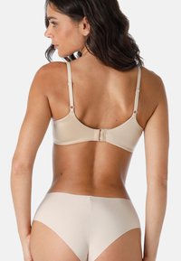 Reggiseno beige con spalline regolabili e chiusura a gancio, abbinato a mutande alte beige coordinate, dalla texture liscia e dal design semplice.