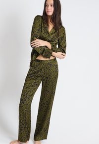 Groene pyjama set met een patroonontwerp en zwarte en oranje accenten. Zachte stof, lange mouwen en losvallende broek.