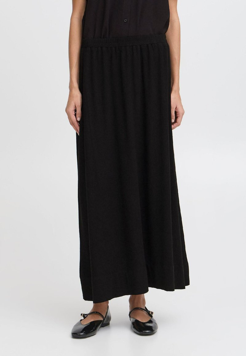 Jupe maxi noire avec une taille élastique, en tissu doux et à la coupe fluide, tombant jusqu'aux chevilles, assortie à des ballerines noires.