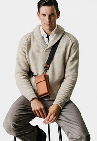 Beige ribbed knit sweater with a shawl collar, paired with light gray checkered trousers and a brown leather crossbody bag.