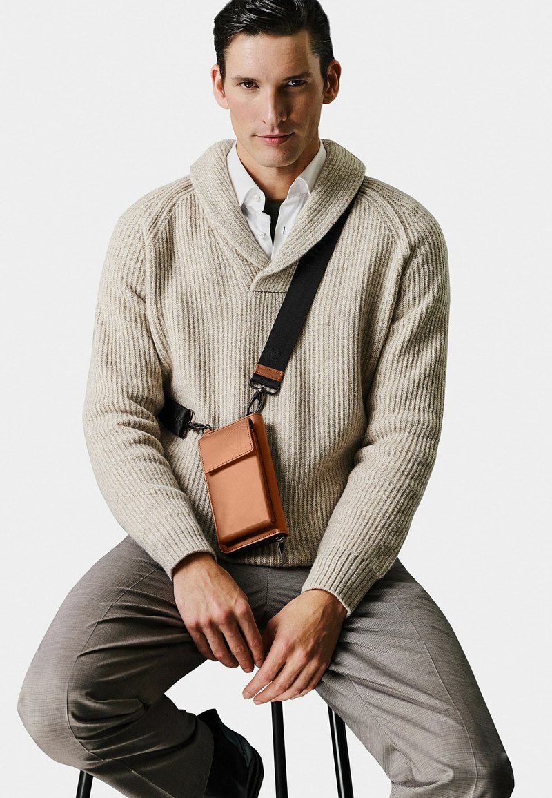 Beige ribbed knit sweater with a shawl collar, paired with light gray checkered trousers and a brown leather crossbody bag.