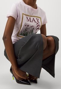 Rosa kortärmad t-shirt med blommig grafik och texten "MAX & CO", tillsammans med grå vida byxor och svarta lackskor med neongröna accenter.