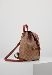 Zaino in pelle marrone con motivo, chiusura a coulisse, tasca laterale con zip e una tracolla e manico marrone-rosso.