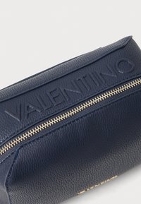 Temno modra usnjena torba z reliefnim logotipom "VALENTINO", z zlatim zadrgo in kontrastnim modrim šivom ob robovih.