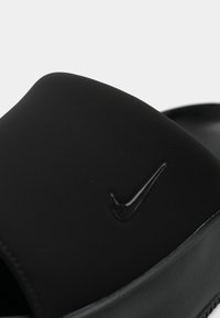 Μαύρη σαγιονάρα με λείο, ματ υφή; διαθέτει ένα εξέχον μαύρο λογότυπο Nike στο επάνω μέρος. Η σόλα έχει ελαφριά υφή πρόσφυσης.