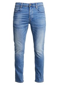 Světlé modré džíny z denimu s tapered střihem, které mají vybledlé části, klasický pětikapsový styl a jedno knoflíkové zapínání v pase.