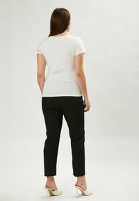 Witte korte mouwen t-shirt met kantaccenten op de schouders, gecombineerd met zwarte slim-fit broeken en witte hakken.