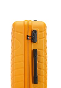Valise rigide de couleur jaune vif, avec une surface texturée, une fermeture éclair noire et un verrou à combinaison, ainsi qu'une seule poignée latérale.