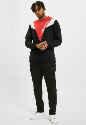 Black sweatshirt with red and white angular color blocks, featuring logo. Paired with black cargo pants and white sneakers.