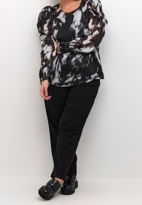 Czarna i biała wzorzysta bluzka z plisowaniem i bufkami, w połączeniu z czarnymi spodniami i masywnymi czarnymi butami. Gładka faktura materiału.