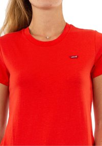 Camiseta roja de manga corta hecha de algodón con escote redondo. Presenta una pequeña etiqueta del logo de Levi's en el lado izquierdo. Textura suave.