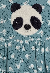 Světle modré šaty s nášivkou pandy. Tkanina má květinové vzory a tečky, s volánkovým lemem a texturovaným designem pandy.