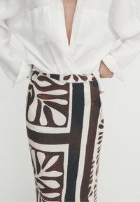 Linnen rok met een gedurfde bruine en witte botanische print, hoge taille en knoopaccenten aan de zijkant. Witte blouse zichtbaar boven.
