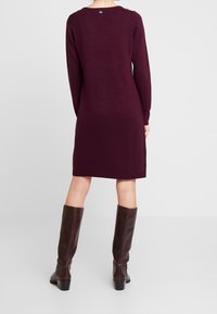 Burgundin värinen neulemekko, jossa on pitkät hihat, ribbireuna ja pyöreä kaula-aukko. Yhdistetty polvisyväisiin, ruskeisiin, kuvioituihin nahkabootseihin.