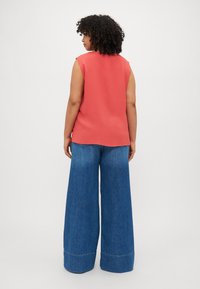 Coral sleeveless top with a relaxed fit, paired with high-waisted wide-leg blue denim jeans, featuring a cuffed hem.